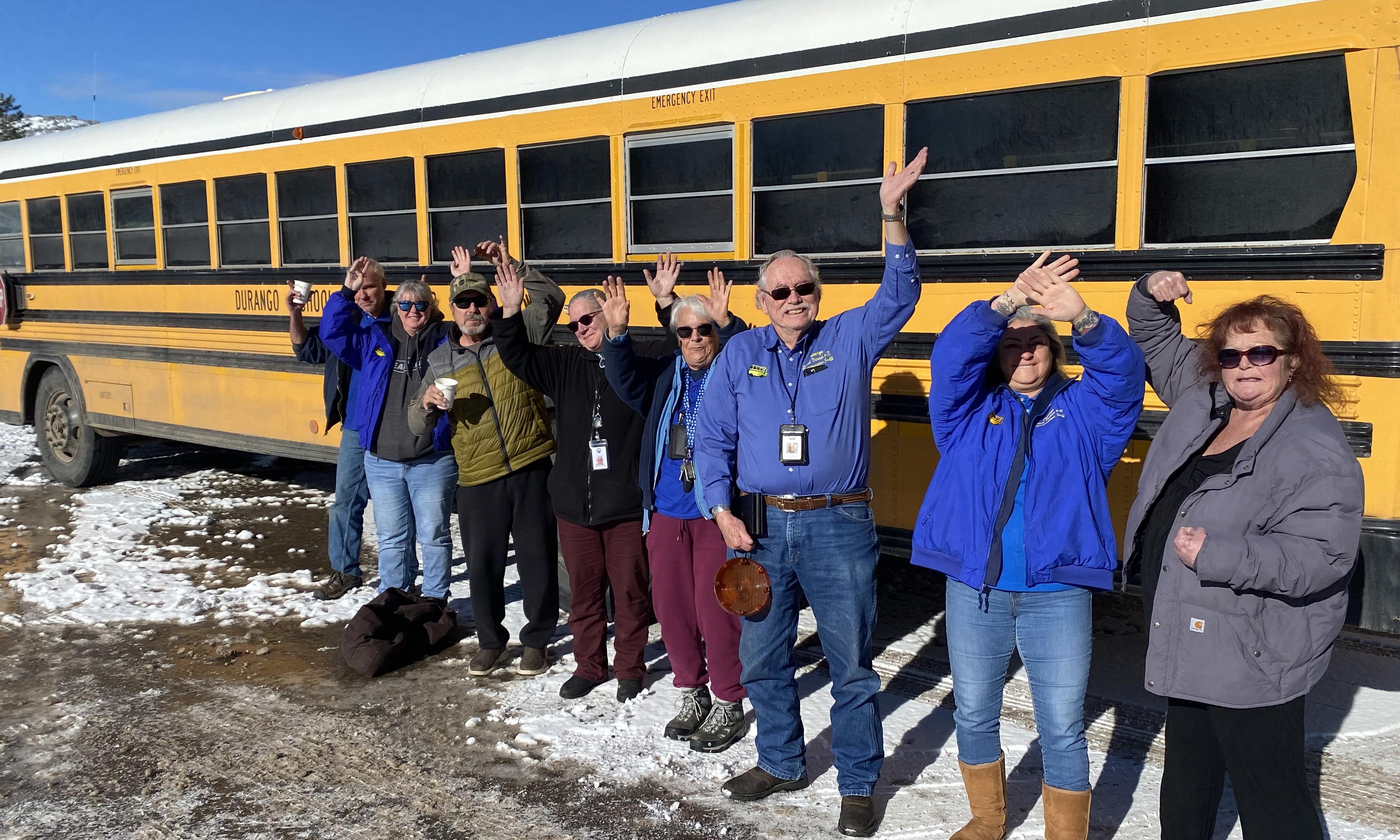 group of bus drivers in front of a bus waving hello